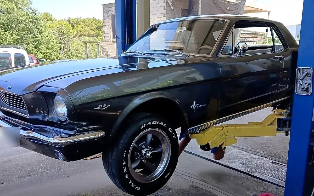 Crni Ford Mustang podignut na dizalici ispred radionice